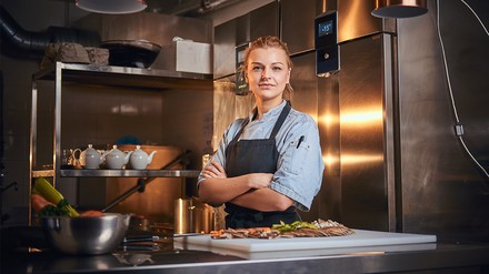 Weibliche Köchin steht mit verschränkten Armen in der Küche