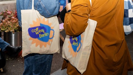 Zwei Menschen mit Coffee Week Jutebeuteln