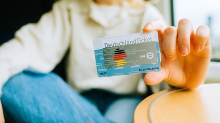 Frau im Zug hält ihr Deutschlandticket in die Kamera