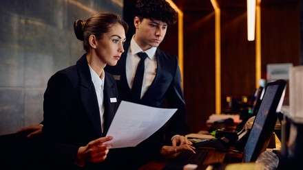 Zwei Hotelmitarbeiter schauen auf einen Computer an der Rezeption