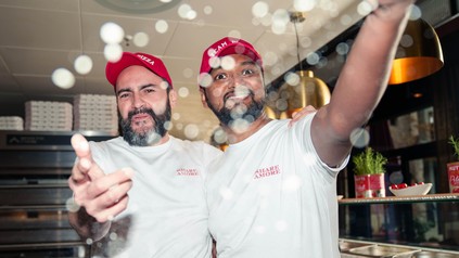 Zwei Mitarbeiter von L’Osteria lachen in die Kamera