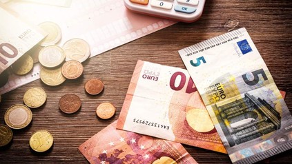 Mehrere Geldscheine und Euromünzen liegen mit einem Taschenrechner auf einem Tisch