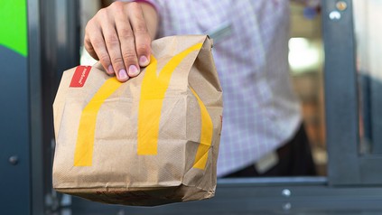 Hand reicht eine McDonald’s-Papiertüte im McDrive durch das Ausgabefenster