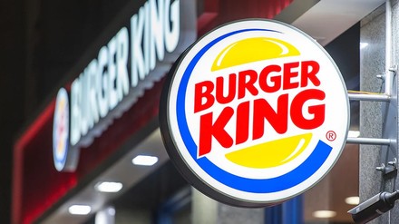 Burger-King-Logo an der Außenfassade eines Restaurants, im Hintergrund die beleuchtete Burger-King-Schrift