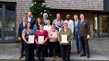 Gruppenfoto der Jubilare und Hotelleitung vor der Traube Tonbach in Baiersbronn; mehrere Mitarbeiter halten Urkunden, im Hintergrund steht ein geschmückter Tannenbaum.