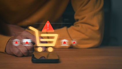 Smartphone mit eingeblendeten Warnsymbolen und Einkaufswagen-Icon – Symbolbild für manipulative Designs und strengere Regeln beim Online-Vertragsabschluss.