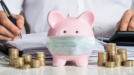 Businessman Calculating Invoice With Piggybank And Coins At Desk