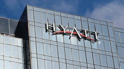 Hyatt-Logo an der Glasfassade eines modernen Hochhauses vor blauem Himmel.