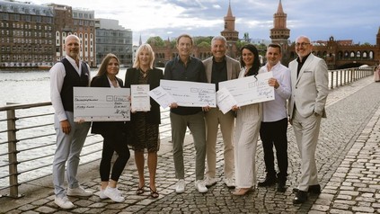 Gruppenfoto der Gewinner des Award der Gastfreundschaft 2025 mit Urkunden und Schecks am Wasser