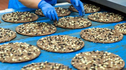 Ein Mitarbeiter am Fließband kontrolliert die Dr. Oetker Schokoladenpizzen