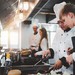 Koch erklärt Auszubildenden in einer professionellen Küche Zubereitungsschritte