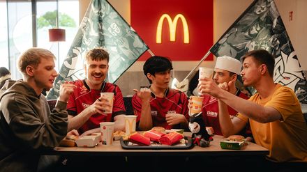Mitglieder eines E-Sport-Teams sitzen in einer McDonald’s-Filiale zusammen an einem Tisch und halten Getränke und Snacks in den Händen