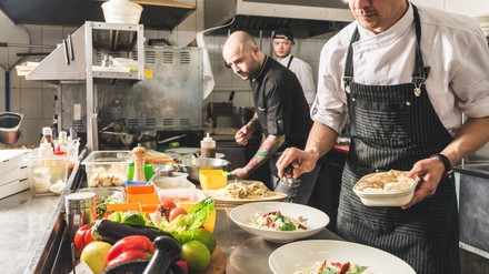 Professionelle Restaurantküche mit drei Köchen, die Speisen anrichten