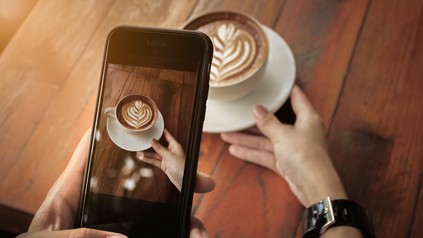 Frau fotografiert Cappuccino mit Smartphone