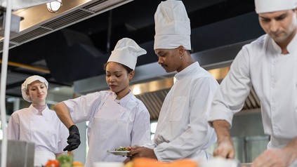 Mehrere Köche bereiten gemeinsam Speisen in einer professionellen Restaurantküche zu.