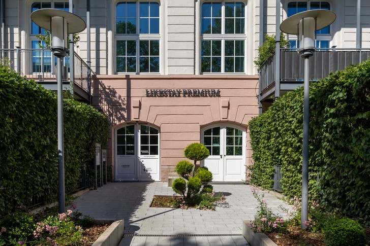 Eingangsbereich des Likestay Premium Baden-Baden mit historischer Fassade, weißen Türen und begrüntem Innenhof.
