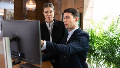 Zwei Hotelmitarbeiter schauen auf einen Computer an der Rezeption