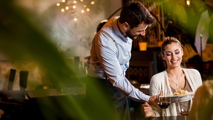 Kellner serviert zwei jungen Frauen beim gemeinsamen Essen in einem Restaurant.