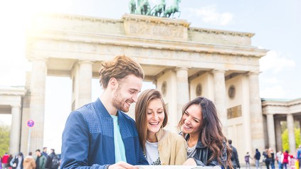Drei Touristen mit Stadtplan vor dem Brandenburger Tor in Berlin