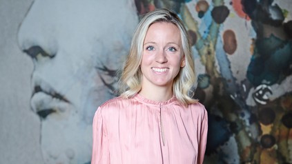 Porträt von Anna Heuer in rosafarbener Bluse vor einer farbig gestalteten Wand