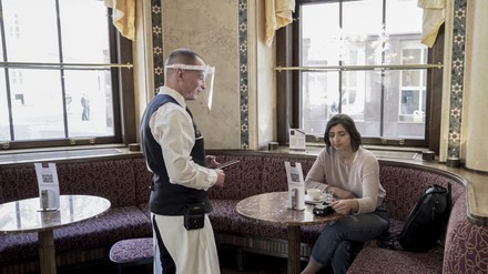 Kaffeehauskellner mit Gesichtsschild bei einem Gast