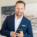 Butler und Concierge Daniel Rudolf im dunkelblauen Anzug mit einem Smartphone in der Hand.