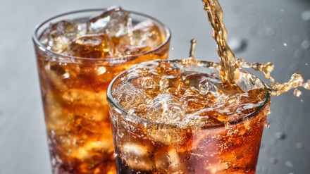 two cups of cola soft drink being poured into glass