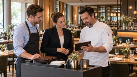 Drei Mitarbeiter aus Service, Küche und Hotel besprechen an einem Tablet den Ablauf im Hotelrestaurant.