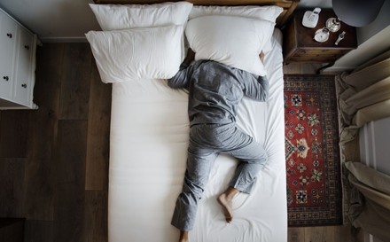 Mann kann nicht schlafen und zieht sich einen Polster über den Kopf.