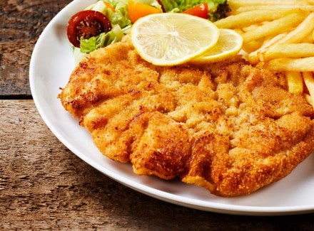 Ein Teller mit Schnitzel, Zitronenscheiben, Pommes und Salat
