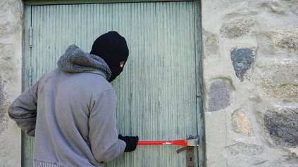 Einbrecher mit Skimaske und Brecheisen bricht Tür auf