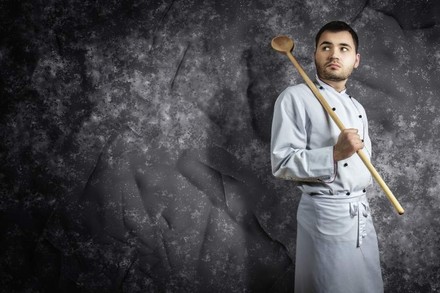 Koch mit riesigem Kochlöffel über Schulter