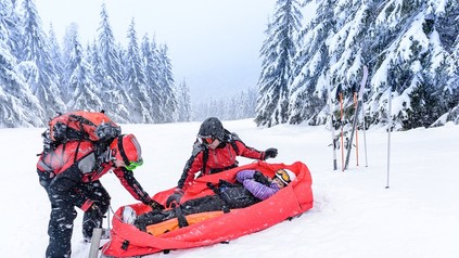 Ski Patrouille mit Rettungsschlitten transportiert verletzte Frau
