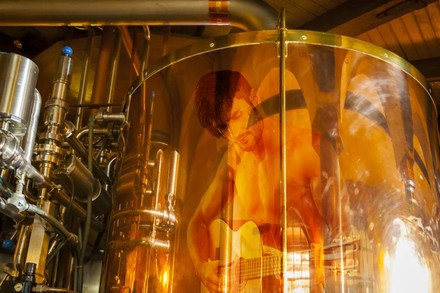 Ein großer Braukessel auf dem sich ein oberkörperfreier Mann mit Gitarre spiegelt