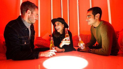 3 junge Leute mit einem Bier in der Hand über einer SAD-Lampe