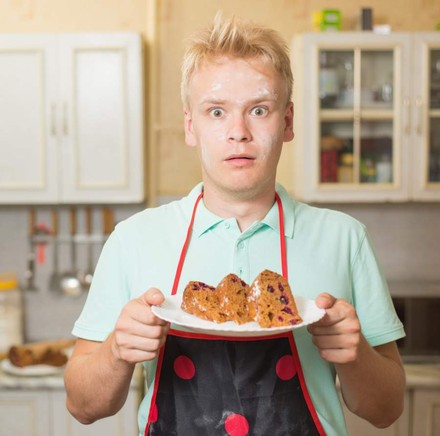 Koch mit Kuchen in der Hand und Mehl im Gesicht