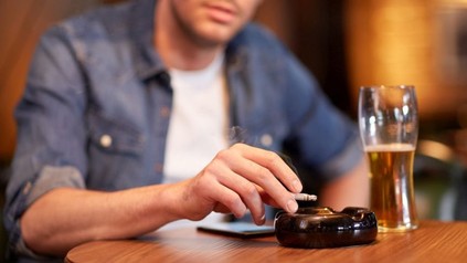 Mann sitzt mit Zigarette und einem Glas Bier in einem Lokal
