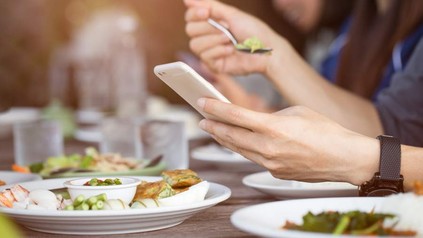 Eine Person beim Essen blickt auf ihr Smartphone