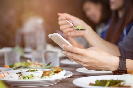 Eine Person beim Essen blickt auf ihr Smartphone