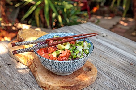 Eine Portion Pokebowl auf einem Holzbrett mit Essstäbchen