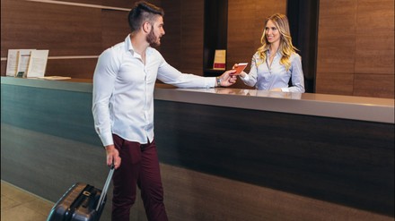 Mann mit Koffer beim einchecken an der Rezeption