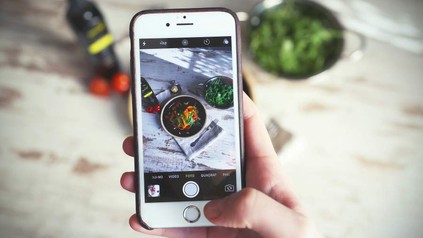 Eine Hand hält ein Smartphone auf dem ein Foto eines leckeren Salats zu sehen ist