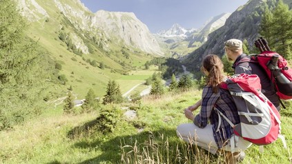 Zwei Wanderer knien auf einer Anhöhe vor einem Bergpanorama