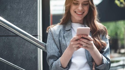 Eine lächelnde Frau blickt auf ihr Smartphone