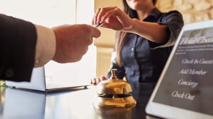 Eine Mitarbeiterin gibt einem Hotelgast an der Rezeption lächelnd eine Karte