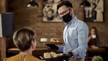 Kellner mit Maske bedient Gast