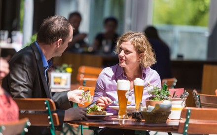 Mann und Frau sitzen zum Mittagessen in einem Gastgarten bei einem Weizenbier.