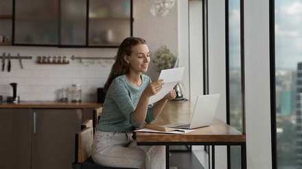 Junge Frau schaut glücklich auf ihre Gehaltsabrechnung