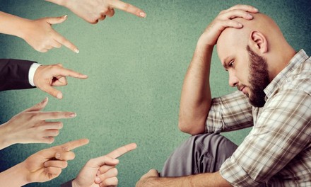 Mann mit Glatze sieht betrübt aus, mehrere Finger deuten auf ihn