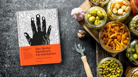 Das Buch „Das Noma-Handbuch Fermentation“ auf einem Tisch liegend neben Einmachgläsern